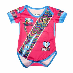 May include: Pink baby bodysuit with blue trim and short sleeves. Features a Guatemalan flag and a colorful geometric design. The text "Guatemala" and "Guile" are visible on the bodysuit. Size M/M.