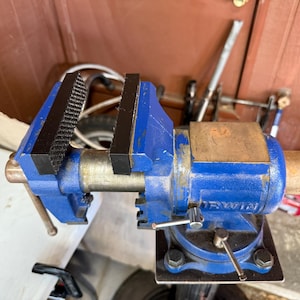 May include: A blue and silver metal bench vise with black jaws. The vise is mounted on a black base and has a handle for tightening. The brand name "IRWIN" is visible on the side.