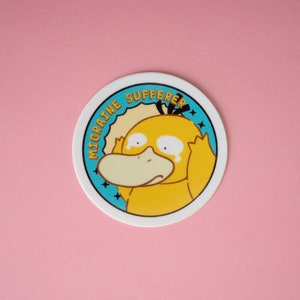 Pode incluir: Um adesivo redondo com um personagem de desenho animado amarelo, Psyduck, segurando a cabe&ccedil;a em ang&uacute;stia. O texto "MIGRAINE SUFFERER" est&aacute; em um c&iacute;rculo turquesa. O fundo &eacute; rosa claro.