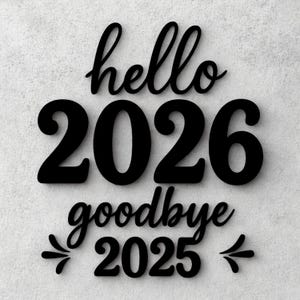 Op de afbeelding: Zwart houten bord met de woorden "hello 2026" boven "goodbye 2025". De cijfers en woorden zijn in een vetgedrukte, gestileerde lettertype. Het bord is gemonteerd op een getextureerde, lichtgrijze muur.