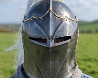 Peut inclure: Un casque en acier poli doté d'une visière pointue avec des fentes oculaires horizontales étroites, orné d'une bordure en laiton le long du front. Le casque est surmonté d'un support métallique central portant un long panache blanc.