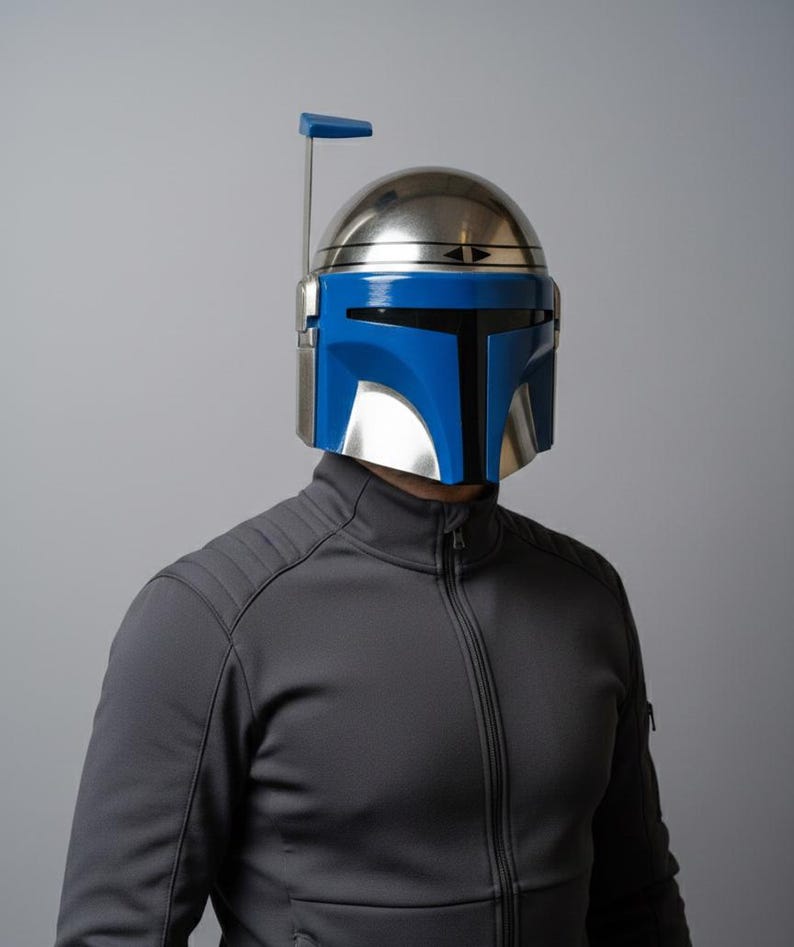 May include: A metallic silver and blue helmet with a vertical antenna. The helmet has a blue visor and a silver dome. The person is wearing a gray zip-up jacket.