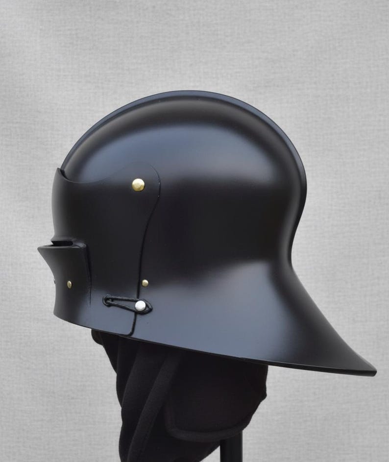 May include: A black, medieval-style helmet with a rounded top and a flared brim. The helmet features brass rivets and a chin strap. The surface has a glossy finish, and the helmet is displayed against a neutral background.
