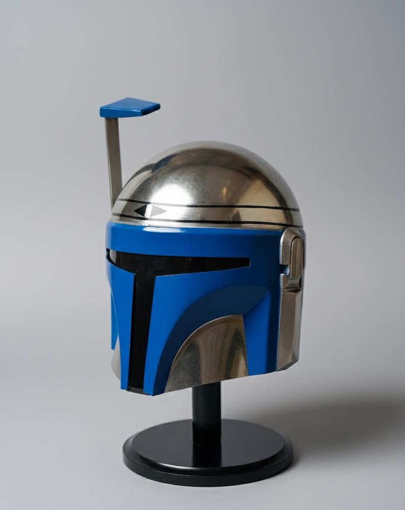 May include: A metallic silver and blue helmet with a black stand. The helmet has a blue visor and a silver dome. A blue antenna extends from the top. The helmet is a replica of a character's helmet from a science fiction film.