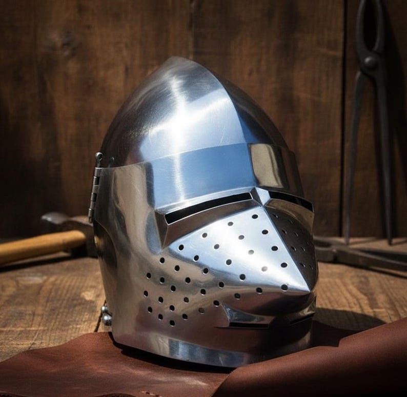 May include: A shiny, silver-coloured medieval helmet with a pointed visor and many small ventilation holes. The metal helmet reflects light. It rests on a brown leather surface, evoking historical or fantasy settings. The helmet is a piece of armour.