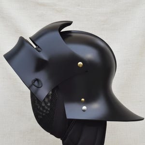 May include: A black metal helmet with a curved visor and a rounded top. The helmet has a series of rivets and a mesh guard. The helmet is likely for historical reenactment or display.