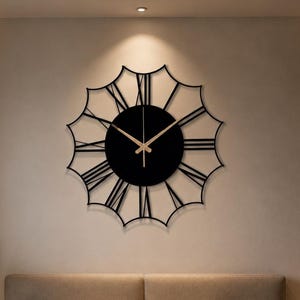 May include: A large, circular wall clock featuring a black central disc with thin, gold-colored hands. The clock has an intricate, open-frame design with black, elongated Roman numerals radiating outward in a starburst pattern from the center.