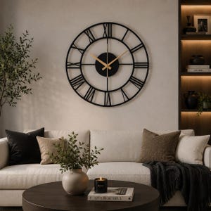 May include: A large circular wall clock featuring a black metal frame with open-work Roman numerals. The center consists of a solid black circular plate with thin, gold-colored hour and minute hands, creating a stark contrast against the dark frame.
