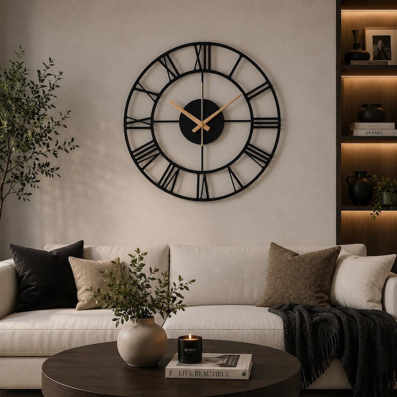 May include: A large circular wall clock featuring a black metal frame with open-work Roman numerals. The center consists of a solid black circular plate with thin, gold-colored hour and minute hands, creating a stark contrast against the dark frame.