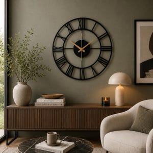 May include: A large, circular wall clock featuring a black metal frame with Roman numerals and thin, gold-colored hands. The clock has an open-work design with a central black circular hub, providing a clear view of the wall behind it.