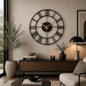 May include: A large, circular wall clock featuring a black metal frame with Roman numerals and thin, light-colored wooden hands. The clock has a central black circular hub and an open-work design that displays the wall color through the frame.
