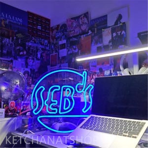 May include: A white ceramic mug with a black handle and the text "But First, Coffee" in a bold, black font. The mug is set against a blurred background, suggesting a cozy setting.