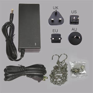 May include: A black power adapter with various plug types labeled UK, US, EU, and AU. Includes a power cord, a metal chain, and a small bag of hardware. The items are arranged on a light gray background.