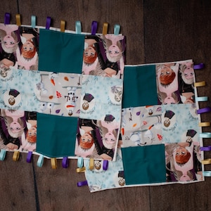 以下が含まれることがあります： 映画アナと雪の女王のキャラクターが描かれたパッチワークデザインの手作りベビーキルト。キルトは青、白、グレーの色合いで、カラフルなリボンで飾られています。