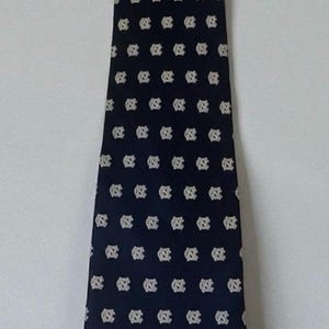 May include: Navy blue tie with a repeating pattern of white interlocking "NC" logos. The tie is displayed against a white background, showcasing its design. A classic accessory for formal or semi-formal attire.