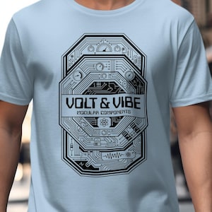 May include: Light blue t-shirt featuring a black and white graphic design. The design includes the text "VOLT & VIBE" above "MODULAR COMPONENTS" and a circuit board-style illustration. The shirt is short-sleeved and made of a soft material.
