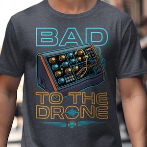 May include: Dark gray t-shirt with a graphic of a synthesizer and the text "BAD TO THE DRONE" in blue and orange. The design includes a skull with headphones. The shirt is made of a soft material.