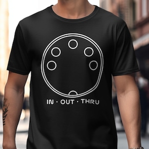 Puede incluir: Camiseta negra con un diseño circular blanco con seis círculos blancos y las palabras "IN • OUT • THRU" en blanco. La camiseta la lleva una persona.