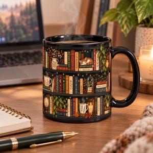 May include: A black ceramic mug featuring a wrap-around illustration of three stacked bookshelves filled with colorful books, a sleeping cat, potted plants, small mugs, candles, and string lights. Steam rises from the top of the mug.