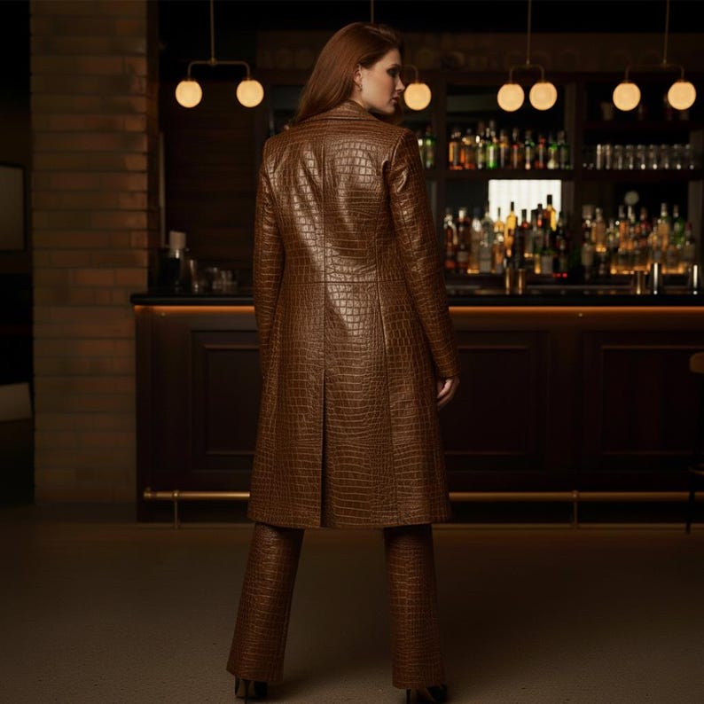 May include: A brown, faux-leather coat and matching pants with a crocodile skin texture. The long coat has a tailored fit and a classic collar. The pants are flared. The outfit is worn in a bar setting.