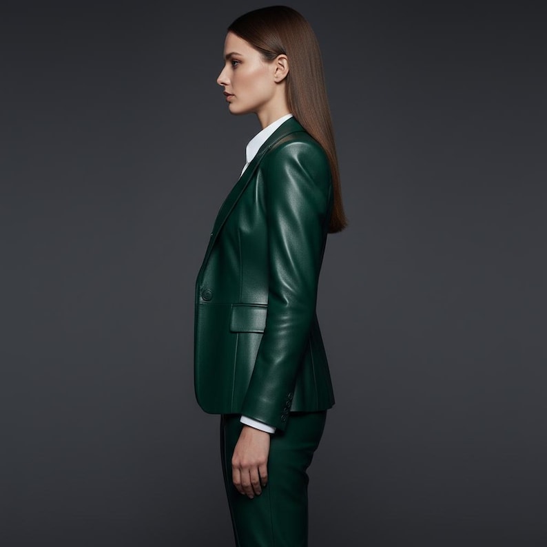 May include: A dark green leather blazer with a single-button closure, paired with matching pants. The blazer features a classic lapel and a tailored fit. A white collared shirt is visible underneath. The outfit is set against a dark gray background.