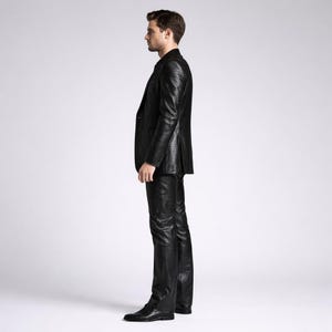 May include: A black suit with a textured pattern. The suit includes a blazer and matching pants. The person is wearing black shoes. The outfit is a formal style.