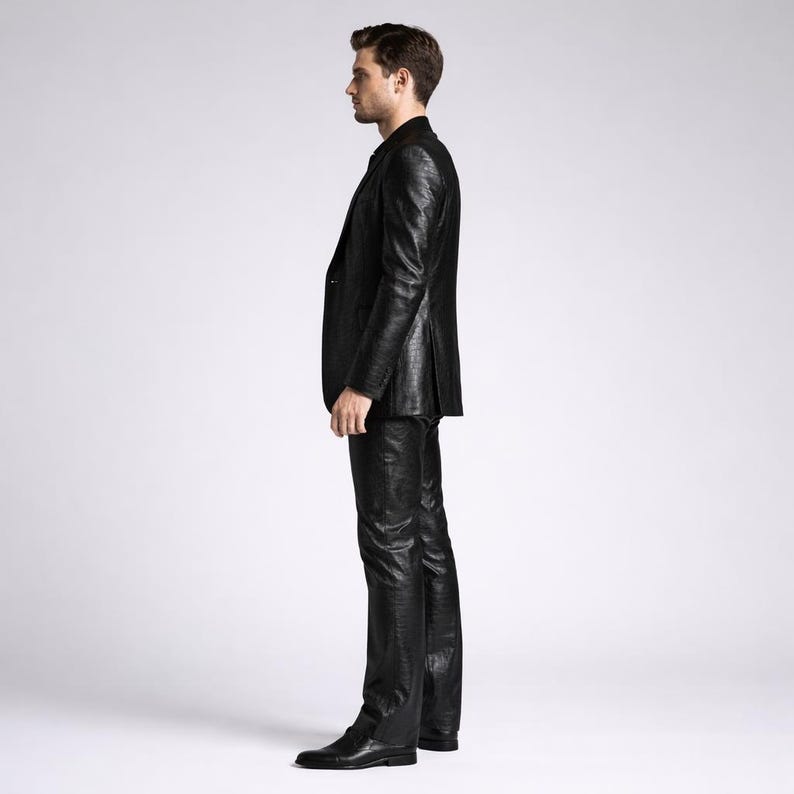 May include: A black suit with a textured pattern. The suit includes a blazer and matching pants. The person is wearing black shoes. The outfit is a formal style.