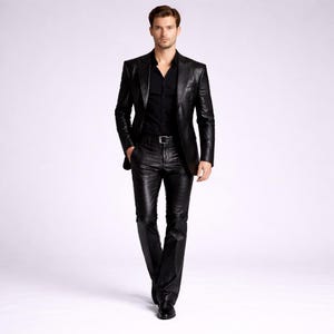 May include: A black leather suit, including a blazer and matching pants, is worn with a black button-down shirt. The suit has a textured appearance and is paired with a silver belt and black shoes. The outfit is set against a plain white background.