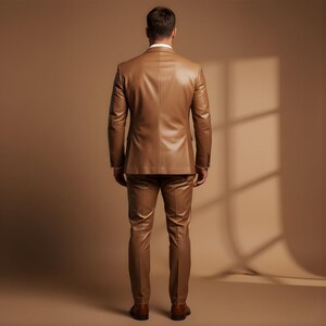 May include: A tan leather suit, consisting of a jacket and pants, is shown from the back. The suit has a tailored fit and a classic design. The person is wearing a white dress shirt underneath the jacket. The background is a solid tan color.