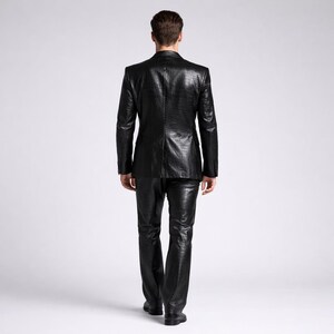 May include: A black, textured suit, including a blazer and pants, is shown from the back. The suit has a reptile-like pattern. The person is walking away from the camera. The suit is a solid black color.