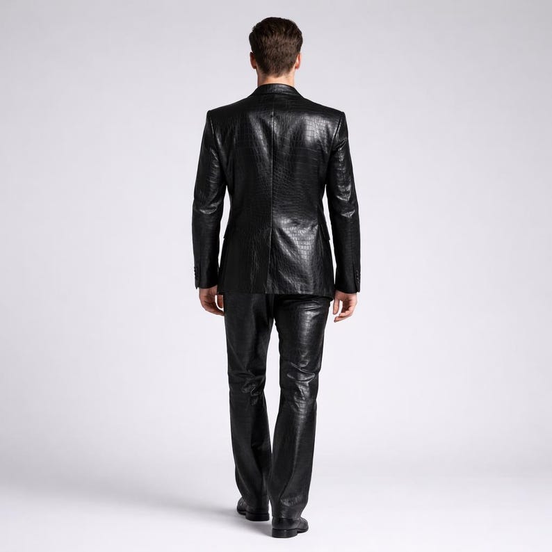 May include: A black, textured suit, including a blazer and pants, is shown from the back. The suit has a reptile-like pattern. The person is walking away from the camera. The suit is a solid black color.