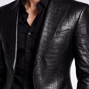 May include: A black leather blazer with a textured, crocodile-like pattern. The blazer has a notched lapel, a chest pocket, and a two-button closure. The blazer is paired with a black button-down shirt.
