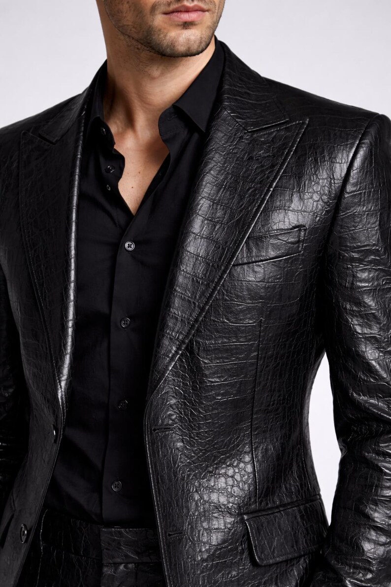 May include: A black leather blazer with a textured, crocodile-like pattern. The blazer has a notched lapel, a chest pocket, and a two-button closure. The blazer is paired with a black button-down shirt.