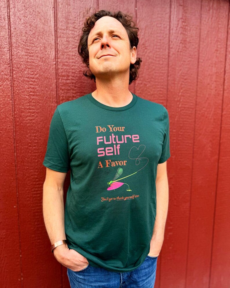 Puede incluir: Una camiseta verde oscuro con el texto "Do Your Future Self A Favor" en rosa y un gr&aacute;fico de lib&eacute;lula. La camiseta tambi&eacute;n incluye la frase "You'll get to thank yourself later". La persona lleva vaqueros azules.