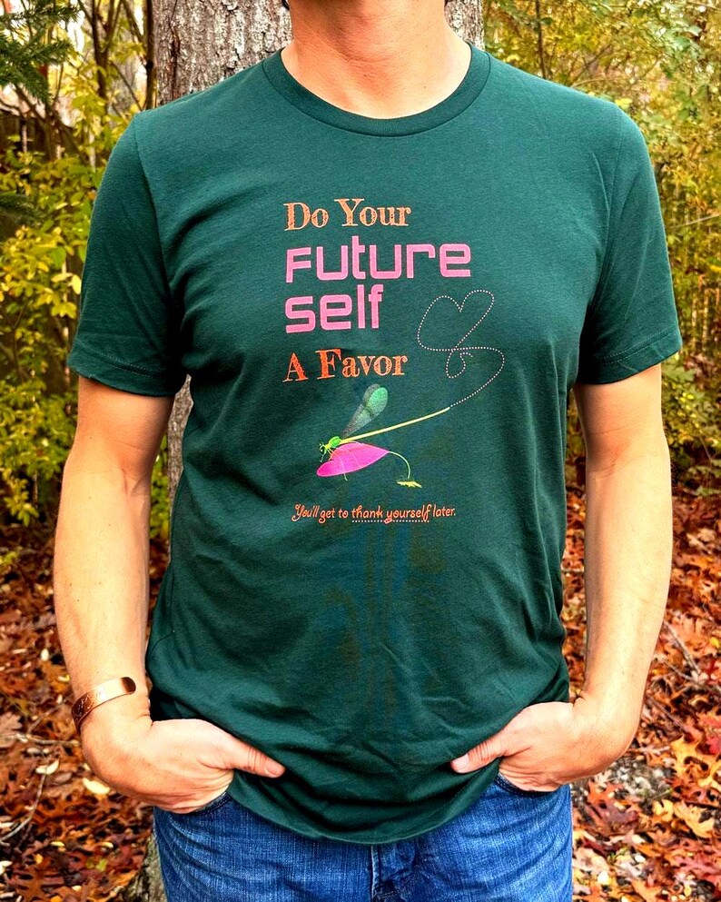 Puede incluir: Camiseta verde oscuro con el texto "Do Your Future Self A Favor" en rosa y naranja. Un gr&aacute;fico de lib&eacute;lula est&aacute; debajo del texto, con la frase "You'll get to thank yourself later." impresa debajo. La persona lleva vaqueros azules.