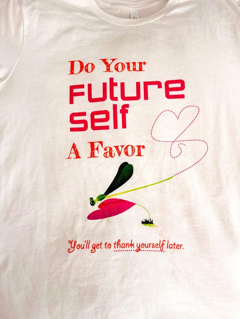 Puede incluir: Camiseta blanca con texto rojo: "Do Your FUTURE self A Favor". Ilustraci&oacute;n de lib&eacute;lula con detalles en rosa, verde y negro debajo del texto. La frase "You'll get to thank yourself later" est&aacute; impresa en rojo.