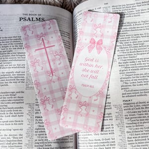 May include: Two pink and white gingham patterned bookmarks with bows and text from Psalms. One bookmark has a cross, the other says "God is within her, she will not fall." The bookmarks are placed in an open Bible.