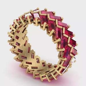Può includere: Un anello a fascia in oro con un motivo continuo di rubini rossi taglio baguette disposti in una configurazione sfalsata e intrecciata. La struttura metallica presenta una finitura in oro giallo lucido con griffe visibili che fissano ogni singola gemma.