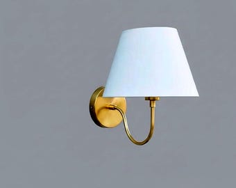 May include: A wall-mounted lamp with a white lampshade and a brass-colored base and arm. The lampshade is conical, and the arm has a curved design. The lamp is designed for indoor use and provides ambient lighting.
