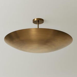 May include: A large, brass-colored ceiling light fixture. The fixture has a wide, shallow bowl shape and a small, circular mounting plate. The light hangs from a short, straight rod. The overall design is minimalist and modern.