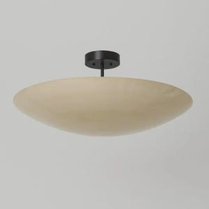 Könnte beinhalten: Eine moderne Deckenleuchte mit einem beigefarbenen, scheibenförmigen Schirm und einer schwarzen Montageplatte. Die Leuchte wird von einer schwarzen Stange abgehängt. Das Design ist minimalistisch und modern.