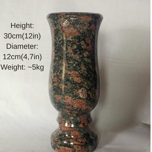 Puede incluir: Un jarrón decorativo de granito rojo Krupsky. Mide aproximadamente 30 cm de alto y 12 cm de diámetro, con un peso de unos 5 kg. El granito presenta un patrón moteado de color rojo, negro y verde.