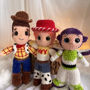May include: Three handmade crochet dolls inspired by characters from the animated film series. The dolls include a cowboy with a brown hat, a cowgirl with a red hat, and a space ranger with a purple and green suit. Each doll has large, expressive eyes.