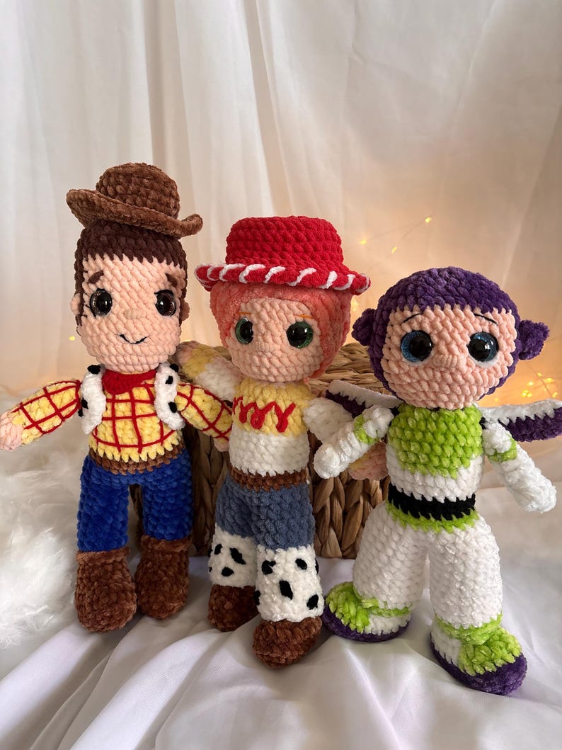 May include: Three handmade crochet dolls inspired by characters from the animated film series. The dolls include a cowboy with a brown hat, a cowgirl with a red hat, and a space ranger with a purple and green suit. Each doll has large, expressive eyes.