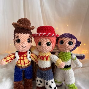 May include: Three handmade crochet dolls inspired by characters from a popular animated film. The dolls include a cowboy with a brown hat, a cowgirl with a red hat, and a space ranger. Each doll has detailed features and vibrant colors.