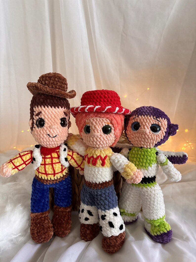 May include: Three handmade crochet dolls inspired by characters from a popular animated film. The dolls include a cowboy with a brown hat, a cowgirl with a red hat, and a space ranger. Each doll has detailed features and vibrant colors.