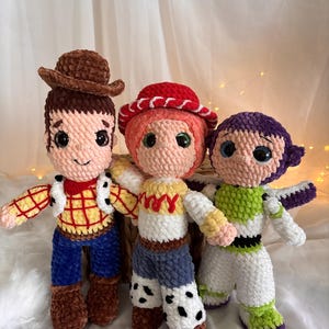 May include: Three handmade crochet dolls inspired by characters from a popular animated movie. The dolls include a cowboy with a brown hat, a cowgirl with a red hat, and a space ranger. Each doll has detailed features and vibrant colors.