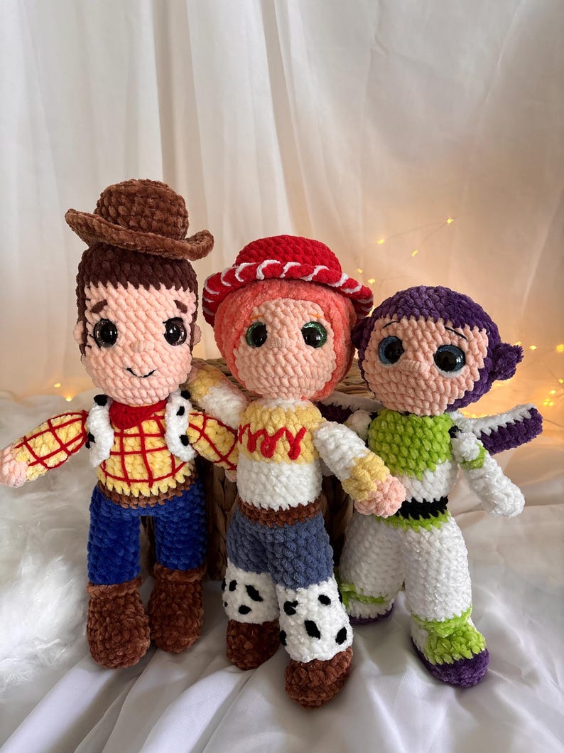 May include: Three handmade crochet dolls inspired by characters from a popular animated movie. The dolls include a cowboy with a brown hat, a cowgirl with a red hat, and a space ranger. Each doll has detailed features and vibrant colors.