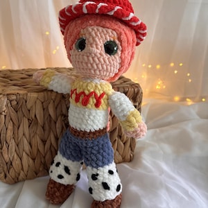 May include: A handmade crochet doll resembling a character from a popular animated film. The doll features a red hat with white trim, a pink face, and a white and yellow shirt. It has blue pants with black spots and brown boots. The doll is approximately 10 inches tall.