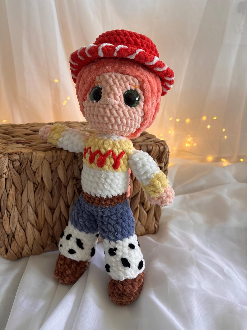 May include: A handmade crochet doll resembling a character from a popular animated film. The doll features a red hat with white trim, a pink face, and a white and yellow shirt. It has blue pants with black spots and brown boots. The doll is approximately 10 inches tall.
